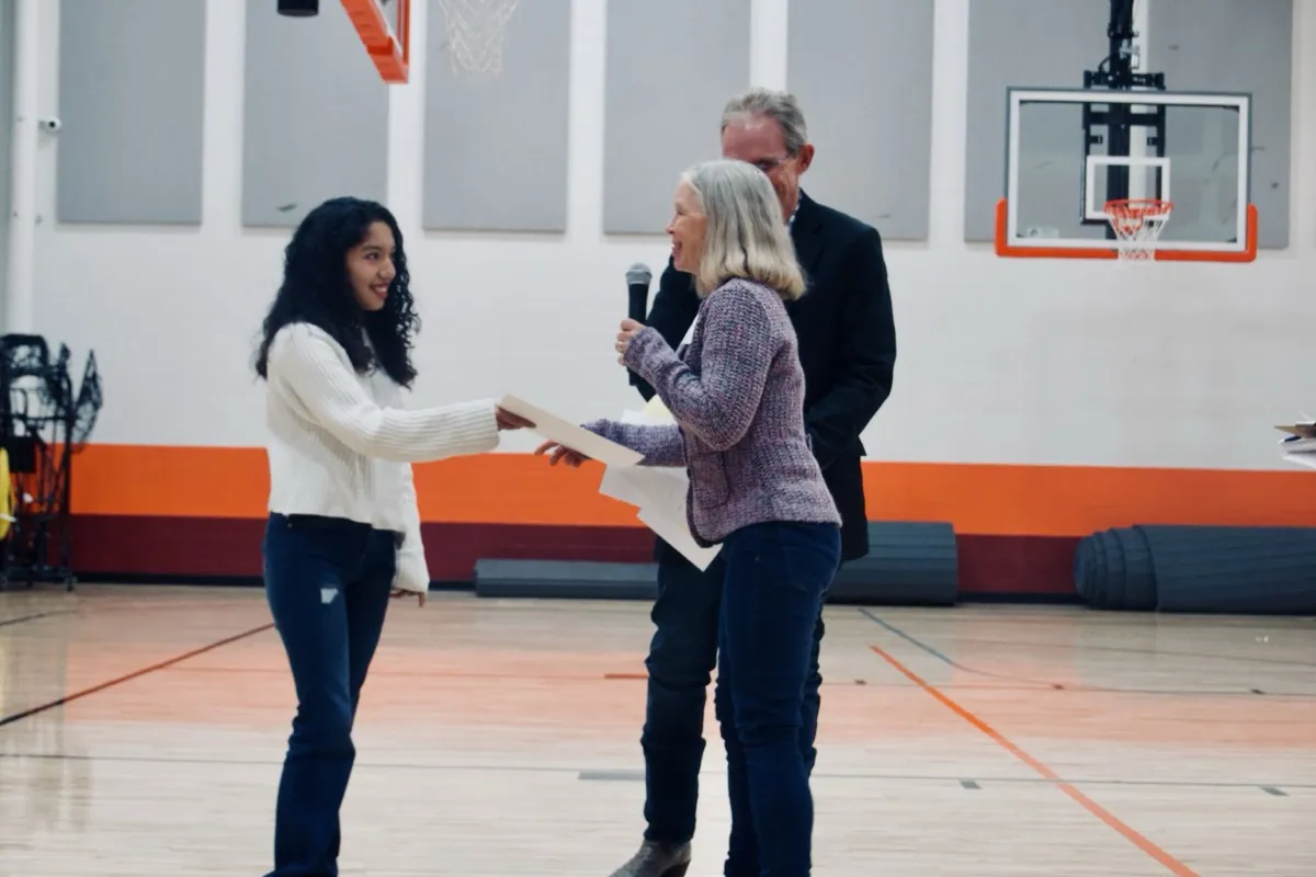 Student receiving a scholarship award from Community Foundation representatives in a school gymnasium
