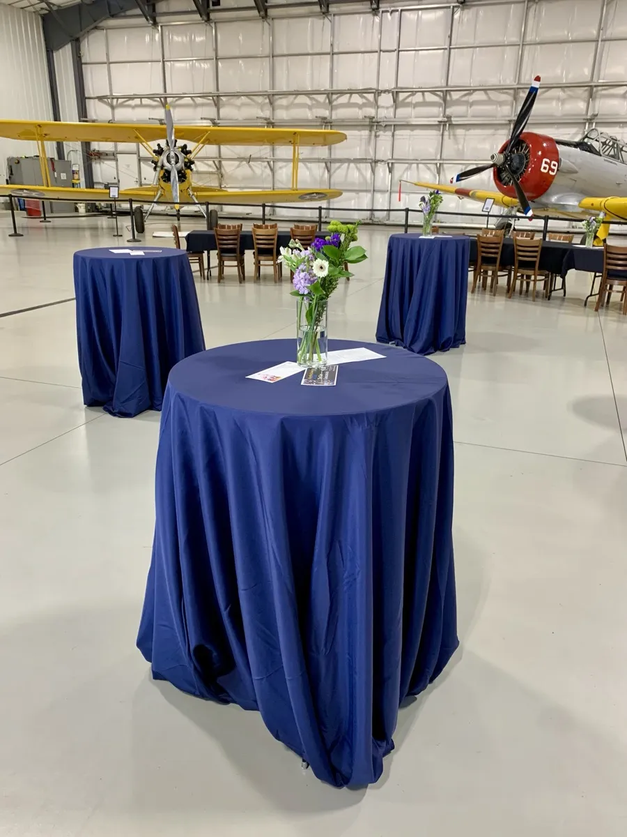 Cocktail tables with flower arrangements set up for a nonprofit event at Teton Aviation hangar